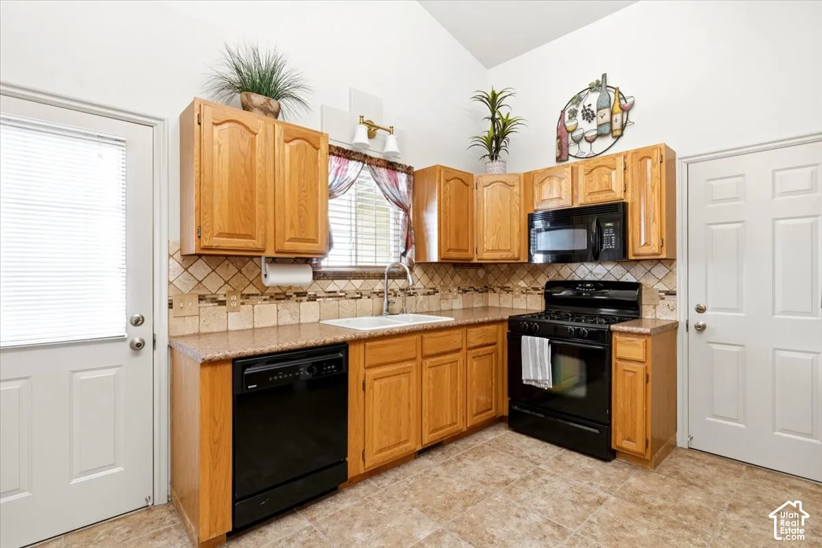 Kitchen featuring light wood cabinetry, a tile backsplash, laminate countertops, a black gas range, and a black dishwasher