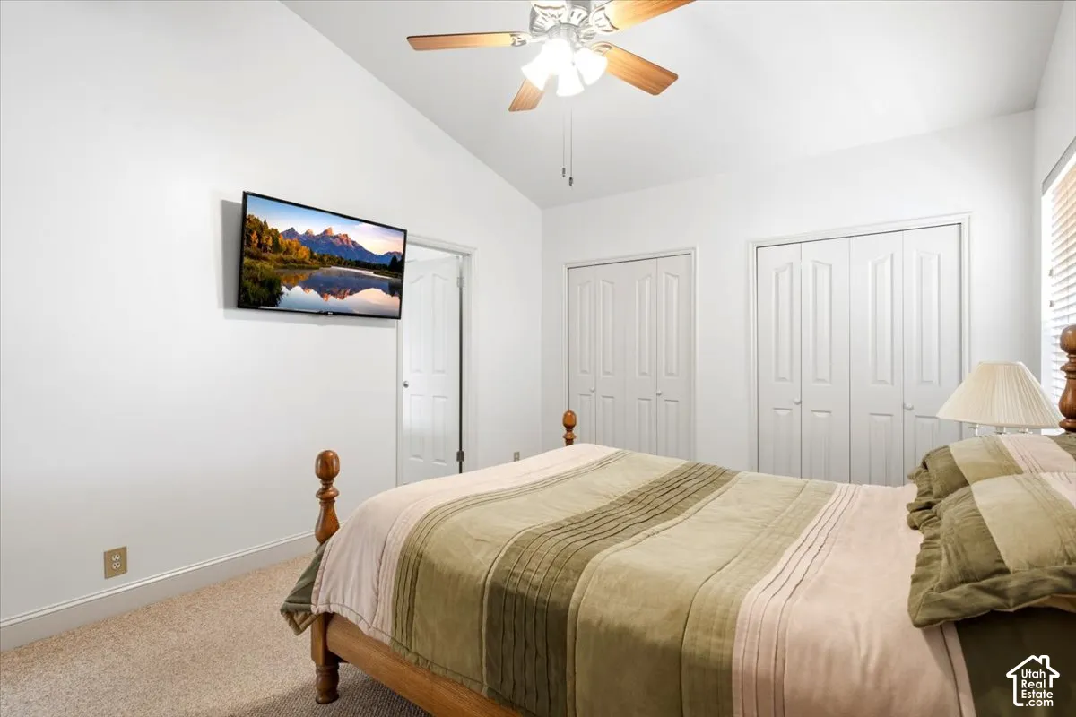 Vaulted ceiling with a ceiling fan and light fixture, two bi-fold closet doors, and carpeted flooring