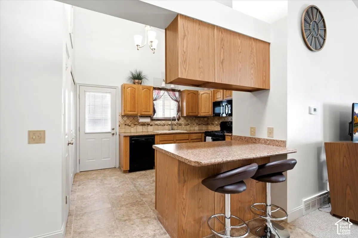 Kitchen featuring wood-finish cabinetry, black appliances, a tile backsplash, and a breakfast bar with a solid surface countertop