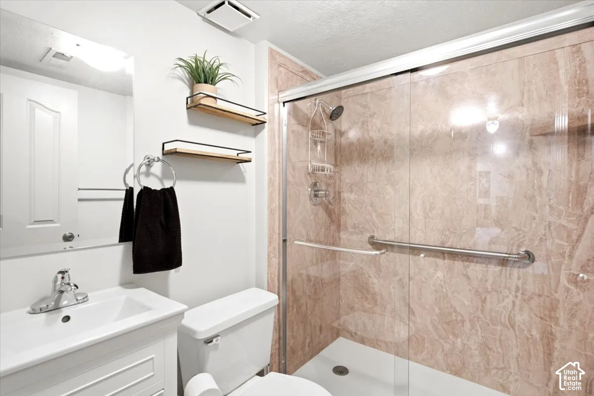 Shower enclosure with sliding glass door, integrated grab bar, and stone-finish wall panels