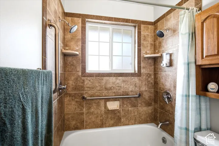 Bathtub with tiled surround, dual shower heads, and built-in grab bars