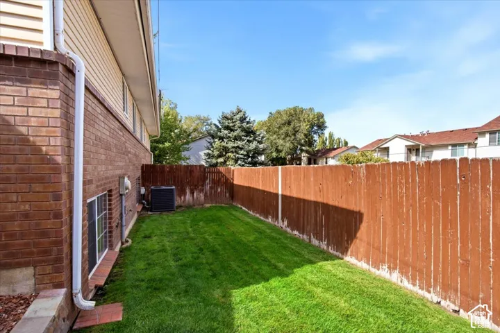 Manicured lawn area with a privacy fence, brick exterior, and white vinyl siding