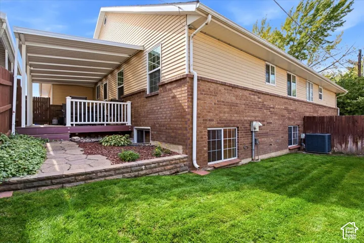 Covered patio deck with white railing, brick exterior, vinyl siding, and grass lawn