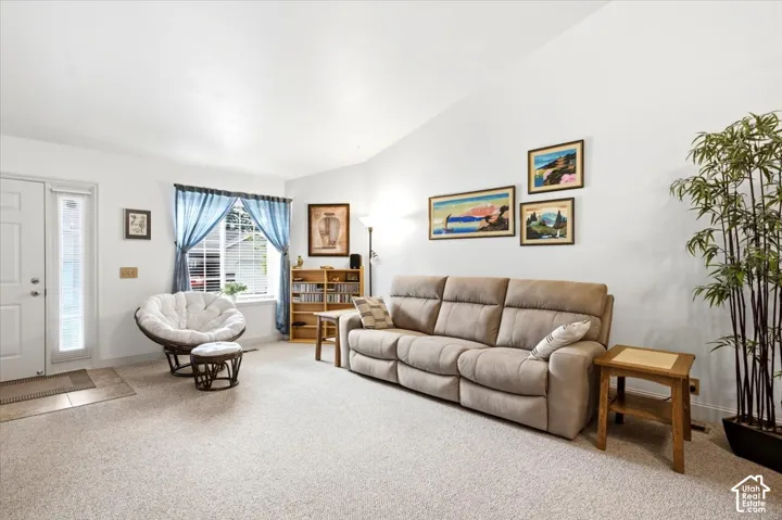 Vaulted ceilings, carpeted flooring, and a large front window with blinds