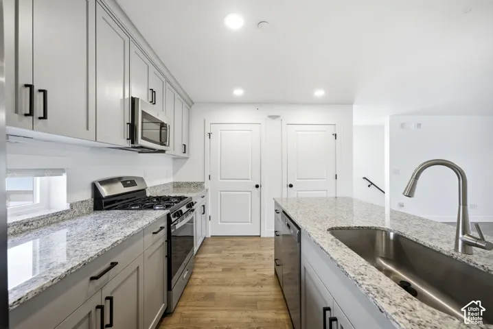 Kitchen featuring an island with an undermount sink, light-toned cabinetry with dark hardware, stainless steel appliances, and light-toned countertops