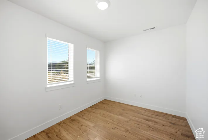 Neutral white walls, wood-finish flooring, two windows with blinds, recessed ceiling light fixture, and white trim