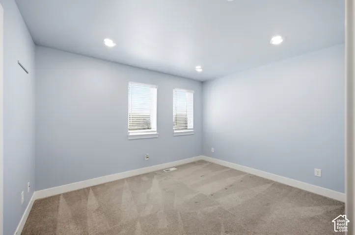 Recessed ceiling lighting, two windows with blinds, light-toned carpeting, and light-colored walls