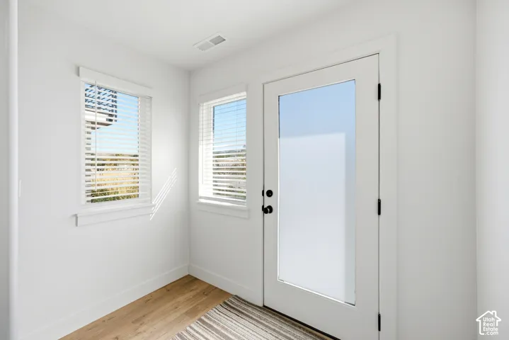 Wood-finish flooring, white walls, two windows with blinds, and a white door with a frosted glass panel