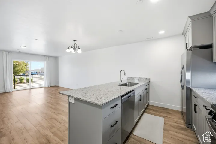 Open-concept living area with wood-finish flooring, a kitchen island featuring a stainless steel sink, granite countertops, and gray cabinetry