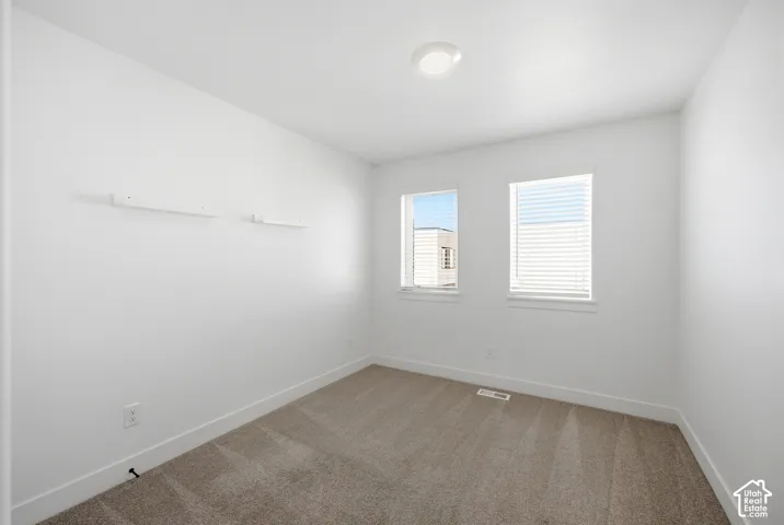 Bright room featuring neutral carpeting, white walls, two windows with blinds, and a flush-mount ceiling light