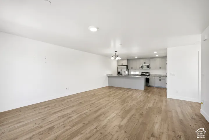 Open-concept living space featuring wood-finish flooring, recessed lighting, and a kitchen with gray cabinetry, stainless steel appliances, and a central island with a sink