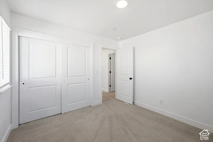 Recessed ceiling light, neutral carpeting, window with blinds, white paneled doors, and white trim