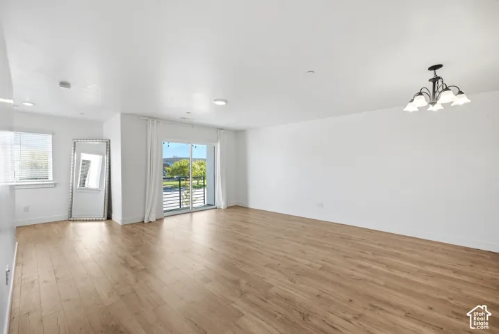 Spacious room featuring light wood-finish flooring, white walls, a multi-pane window with blinds, and a glass sliding door leading to a balcony with black metal railings