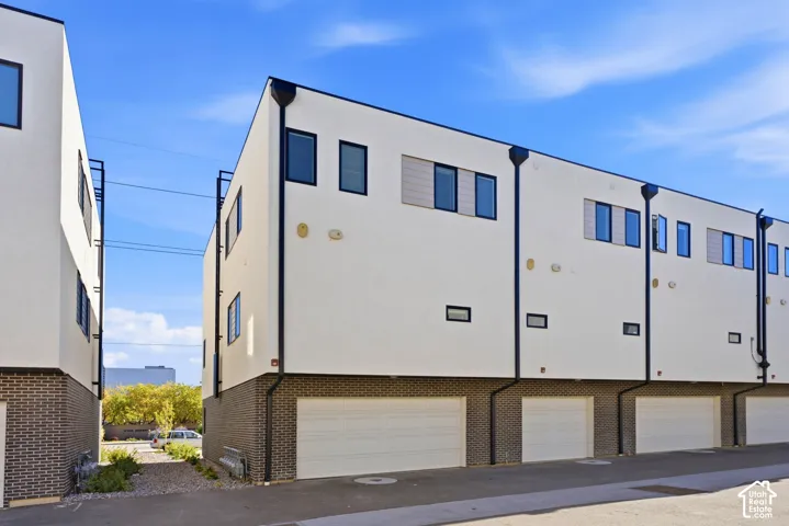 Modern exterior with white stucco siding, dark brick lower facade, multiple garage doors, and dark-framed windows