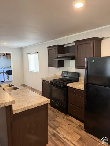 Kitchen featuring dark wood-finish cabinetry, light-toned countertops, black appliances, and wood-finish flooring