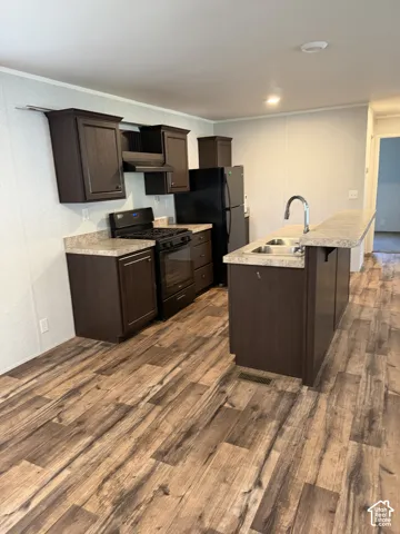 Kitchen featuring dark wood-finish cabinetry, black appliances, wood-finish flooring, and a double-basin sink with a gooseneck faucet