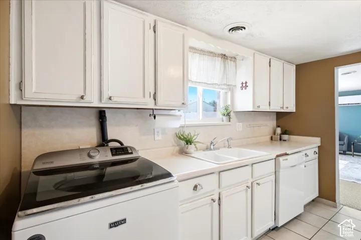White cabinetry with brushed nickel hardware, dual basin sink with chrome faucet, light-toned countertop, and tiled flooring