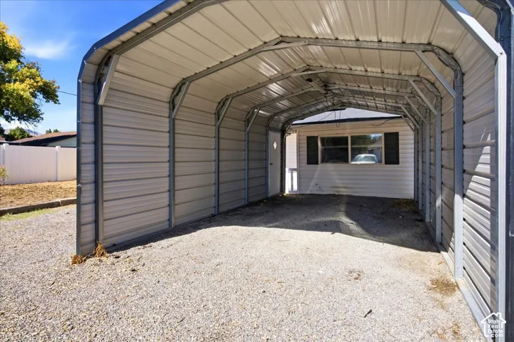 Metal carport structure with a gravel surface and white privacy fencing