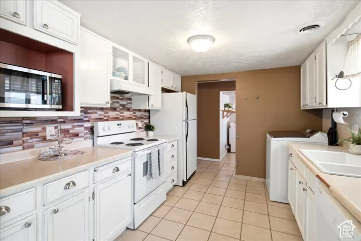 White cabinetry, tile flooring, built-in microwave, integrated kitchen sink, and a tile backsplash