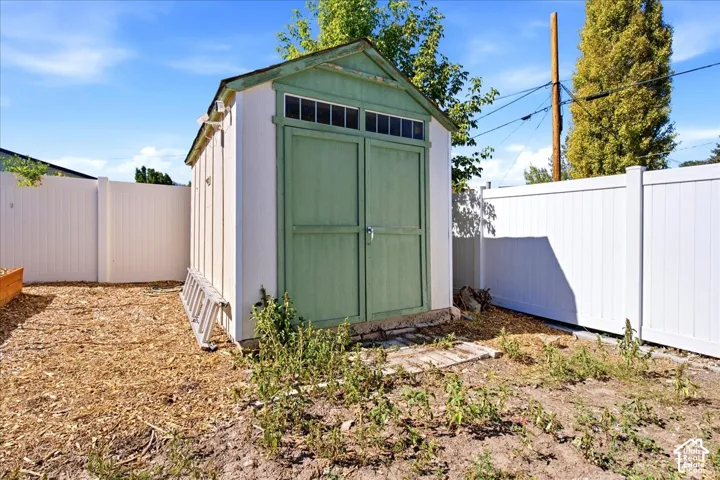 Storage shed with louvered windows and double doors, bordered by white privacy fencing