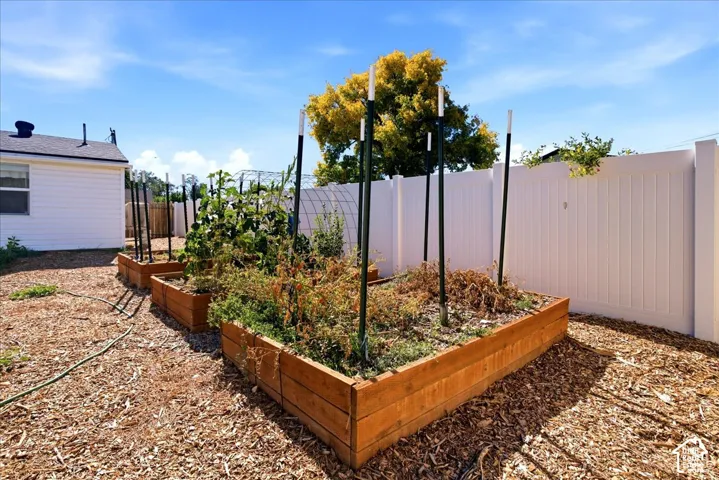 Three raised garden beds, white vinyl privacy fence, and wood chip ground cover