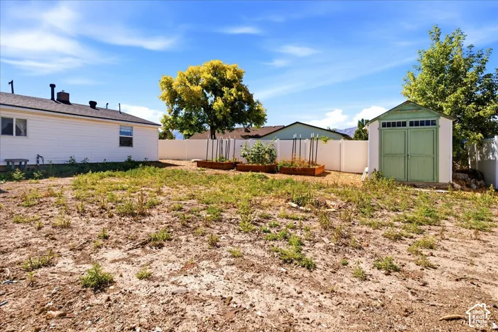 Expansive yard space featuring a storage shed, white vinyl fencing, and raised garden beds