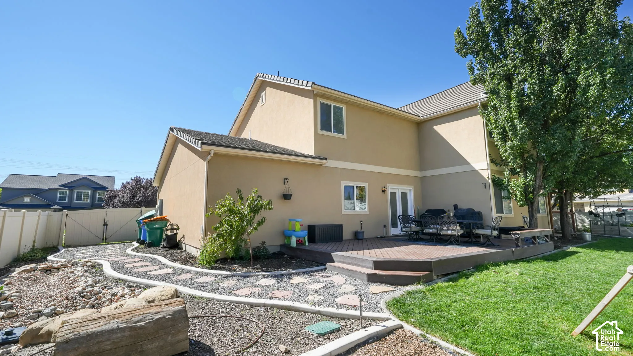 Multi-level composite deck with steps, stucco exterior, white framed windows, and a manicured lawn