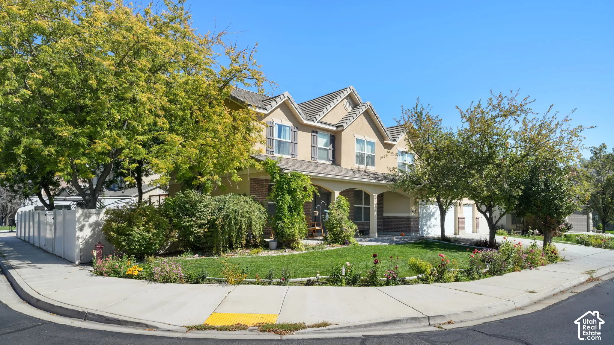 Two-story stucco and brick exterior, covered front porch with columns, mature landscaping, sidewalk, and street frontage