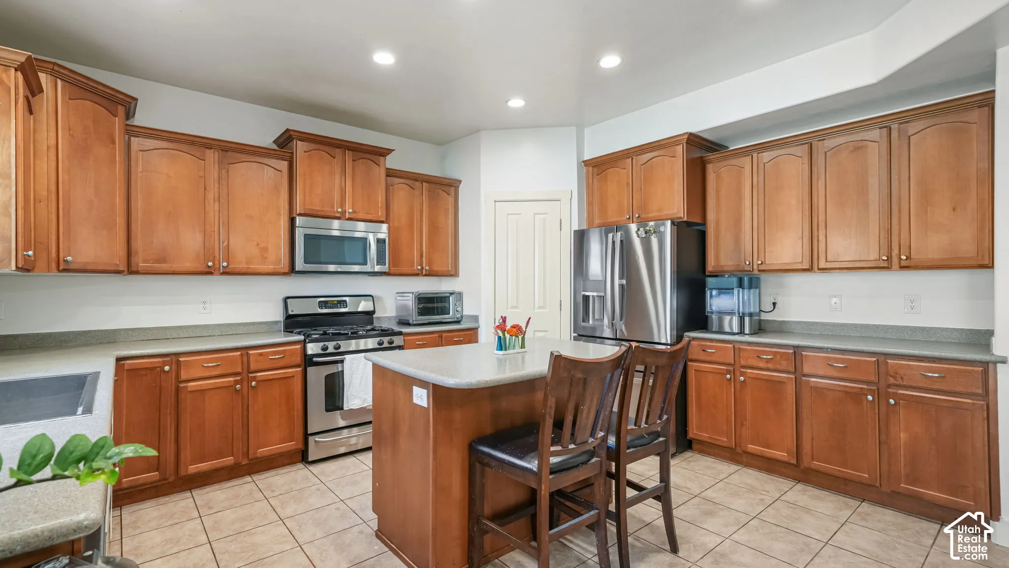 Kitchen featuring wood cabinetry, stainless steel appliances, a center island with countertop seating, and tile flooring