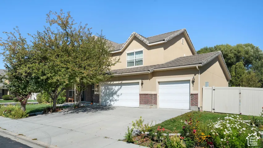 Stucco exterior with brick detailing, asphalt shingle roof, two-car garage, and a privacy fence