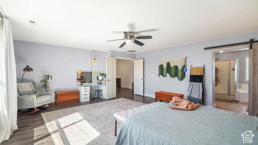 Wood-finish flooring, ceiling fan, white paneled doors, and a barn door entry to a bathroom featuring a walk-in shower and a built-in tub