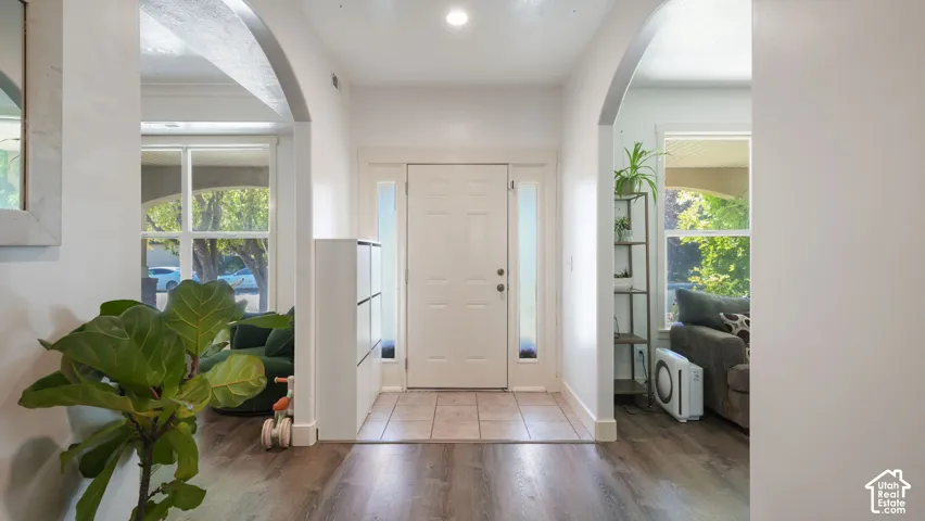 Foyer featuring a white entry door with frosted side lights, arched doorways, and wood-finish flooring