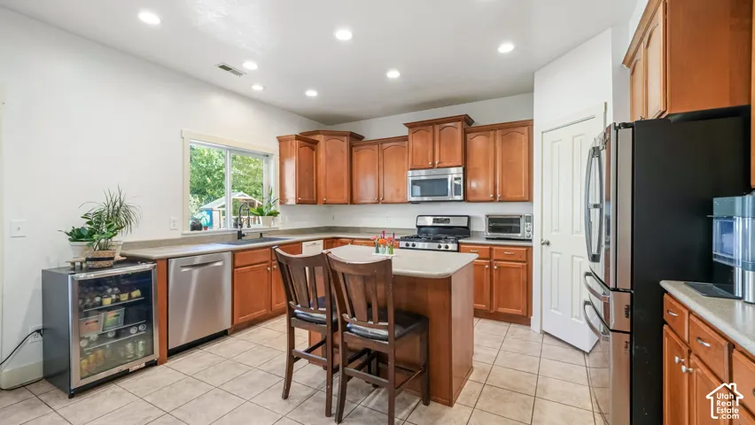 Kitchen featuring wood cabinetry, stainless steel appliances, a center island with seating, tile flooring, and recessed lighting