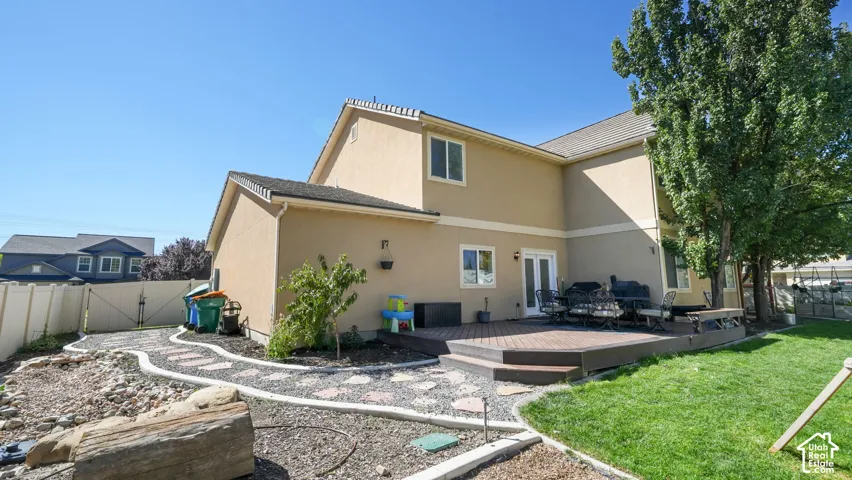 Multi-level composite deck with steps, stucco exterior, white framed windows, and a manicured lawn