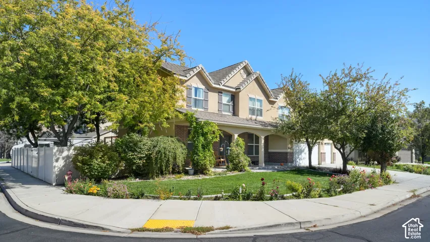 Two-story stucco and brick exterior, covered front porch with columns, mature landscaping, sidewalk, and street frontage