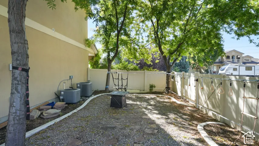 Gravel hardscaping with a decorative fire pit, mature trees, and a privacy fence