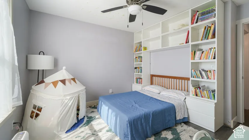 Integrated built-in shelving, wood headboard, overhead ceiling fan, and window with natural light