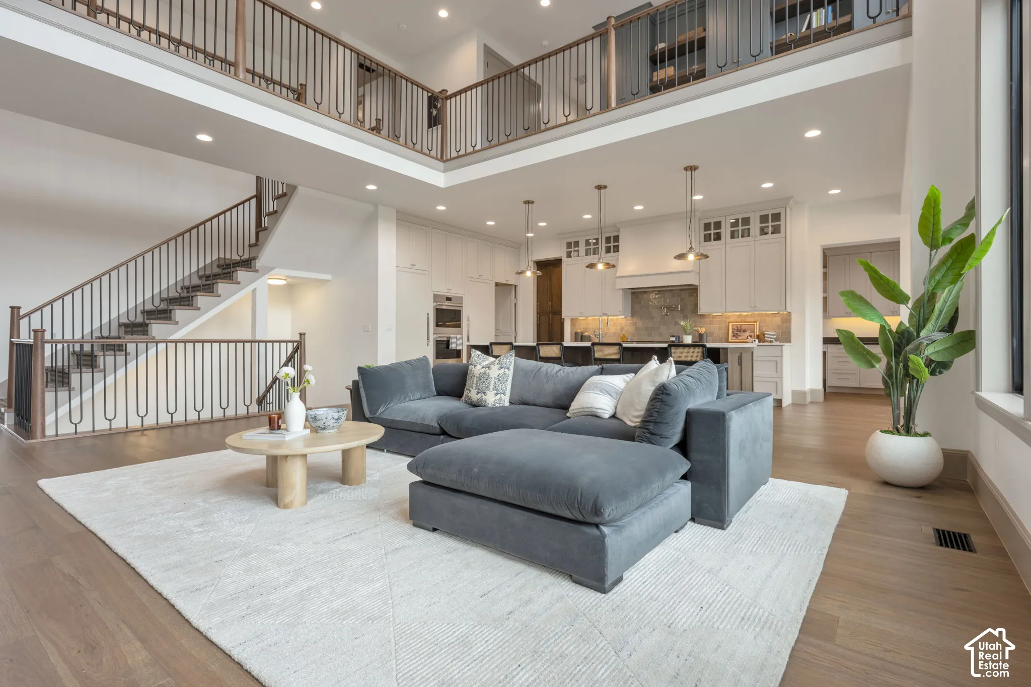 Open-concept living area with high ceilings, wood-finish flooring, and a two-story staircase featuring decorative metal balusters