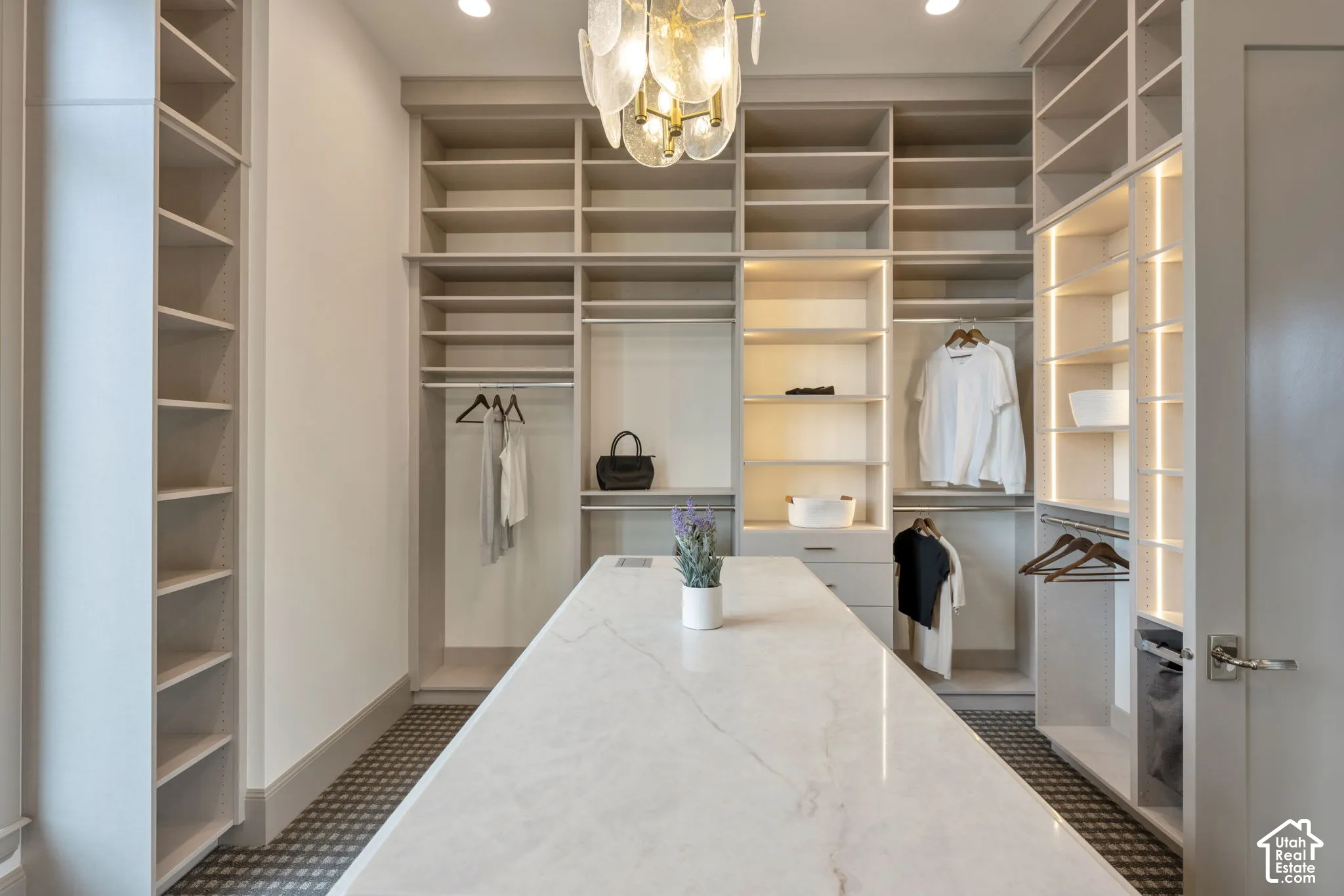 Custom closet system with extensive shelving, integrated hanging rods, a central island with a stone countertop, and recessed lighting