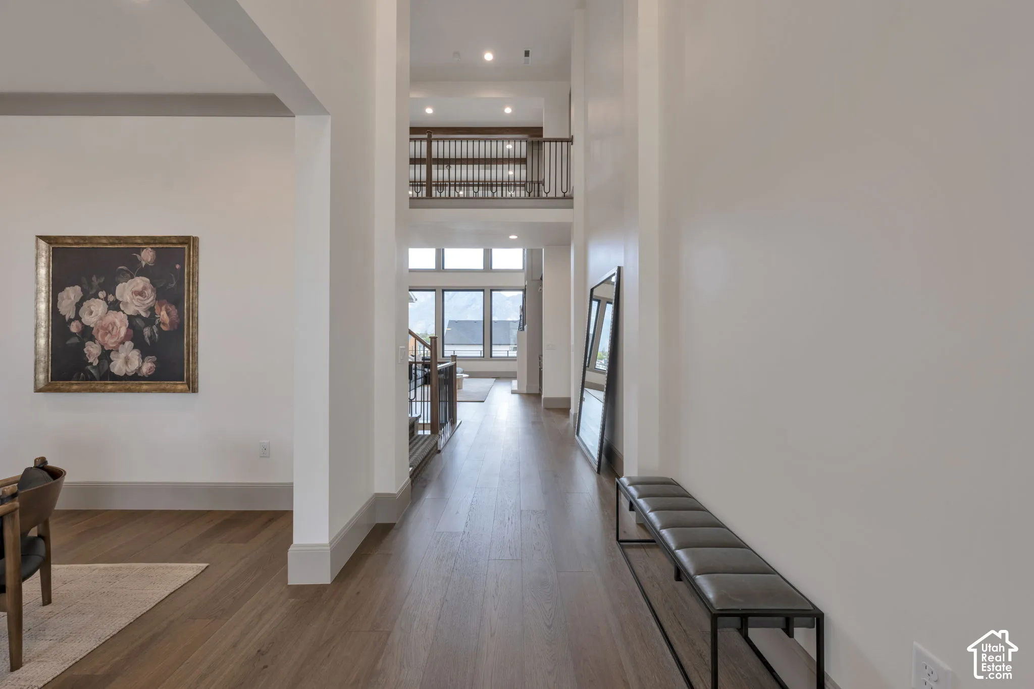Wood-finish flooring throughout, soaring ceilings, upper-level balcony with wood and metal railings, and extensive window placement