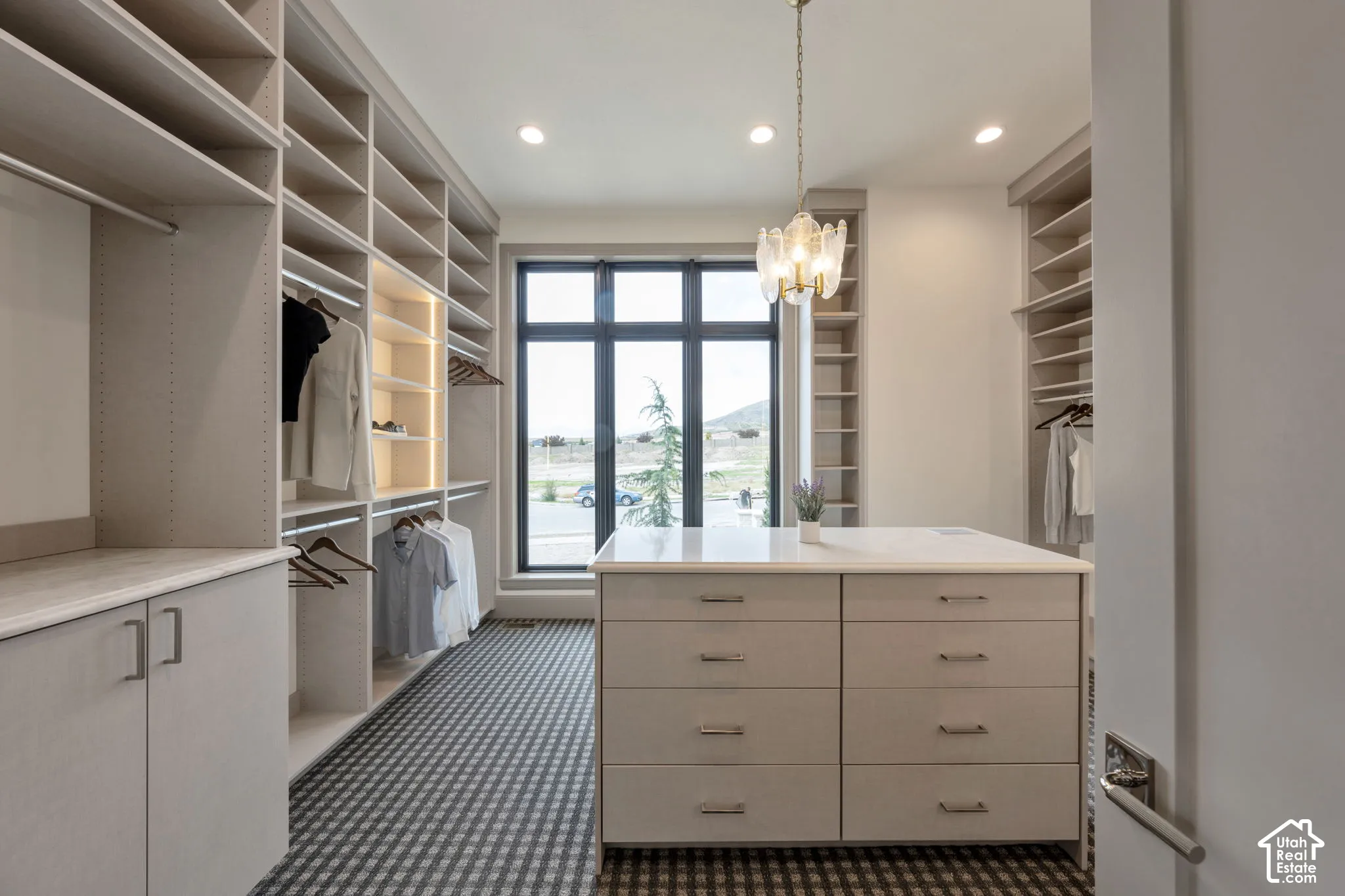 Custom built-in storage with integrated lighting, a central island with drawer storage and stone countertop, a large window with dark trim, recessed lighting, and a decorative ceiling fixture