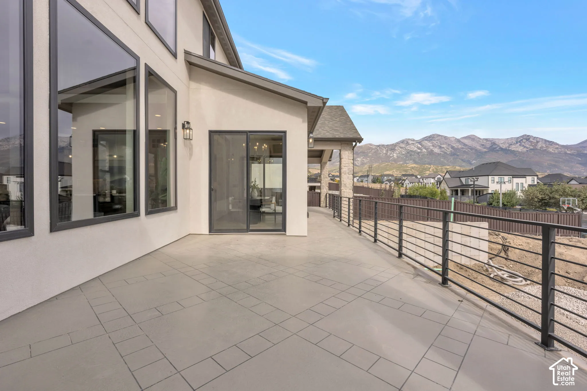 Expansive outdoor patio with patterned tile flooring, contemporary horizontal metal railings, and a sliding glass door