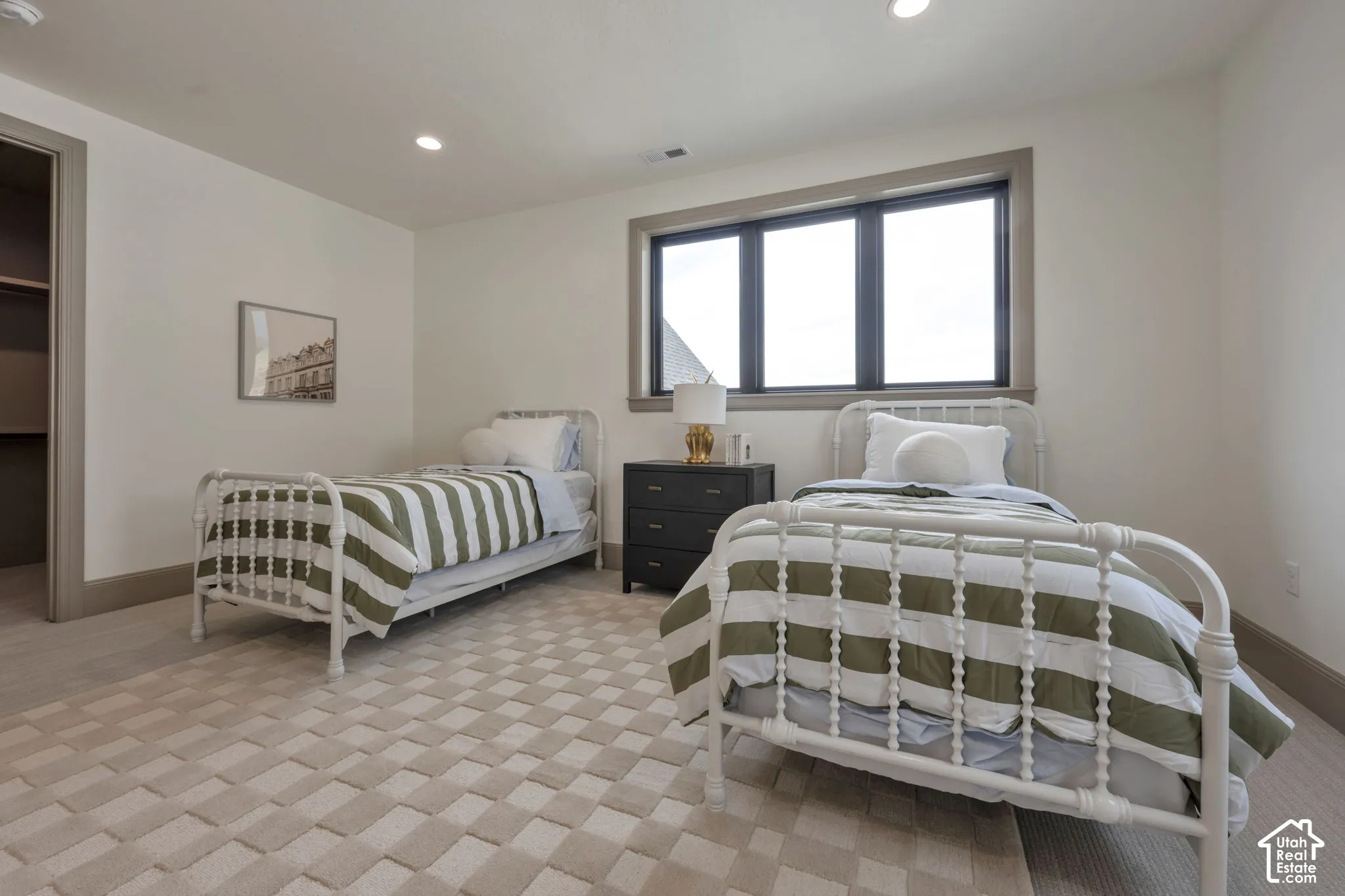 Recessed lighting, large window with dark trim, neutral wall color, patterned carpet flooring, and an open closet with built-in shelving