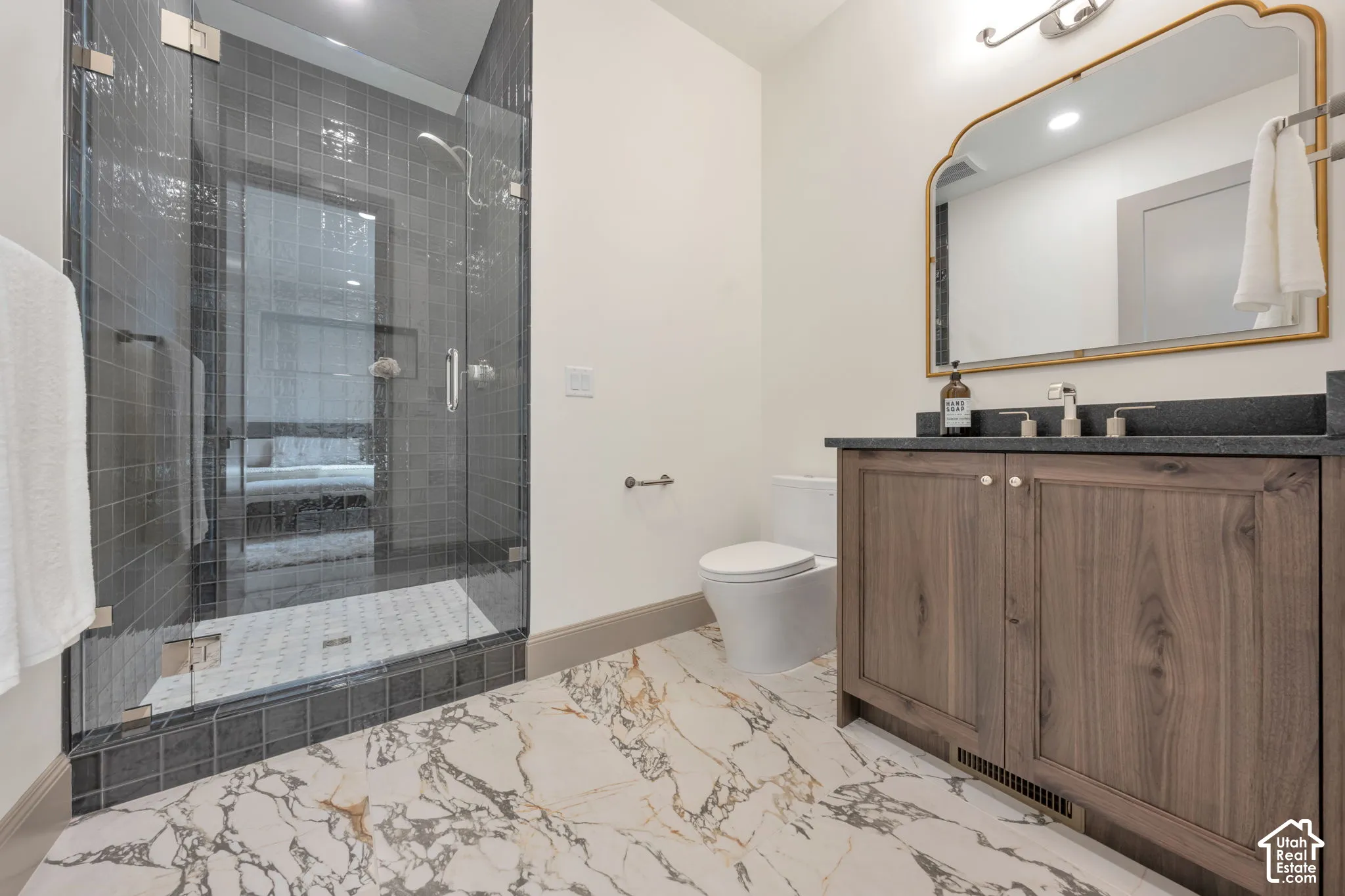Walk-in shower with glass enclosure, wood-finish vanity with dark countertop, large decorative mirror, and marble-look flooring