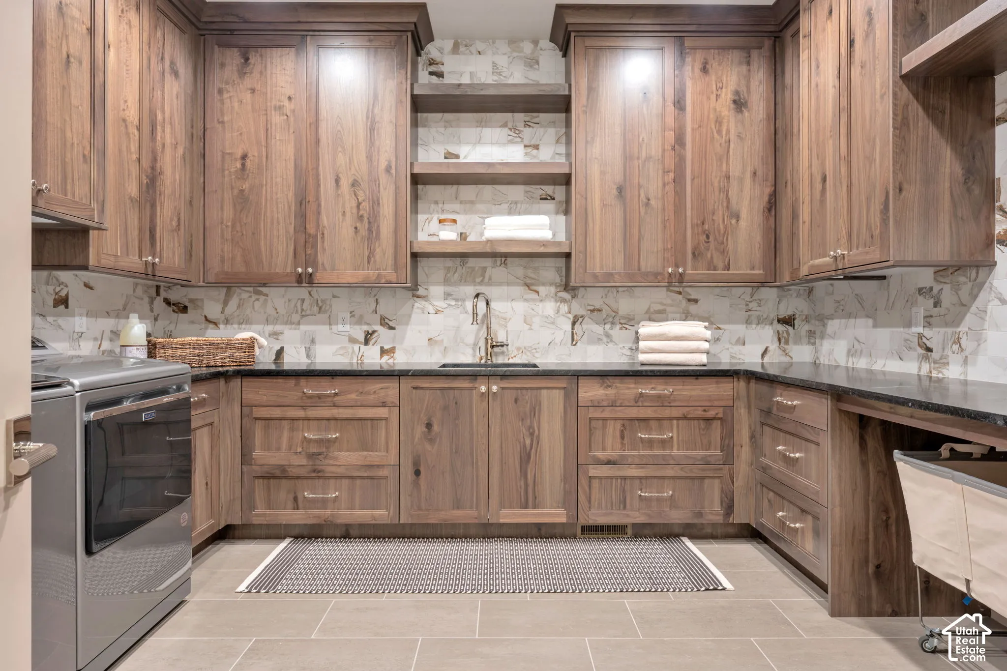 Custom wood cabinetry, black countertops, tile backsplash, built-in shelving, and large format floor tiling
