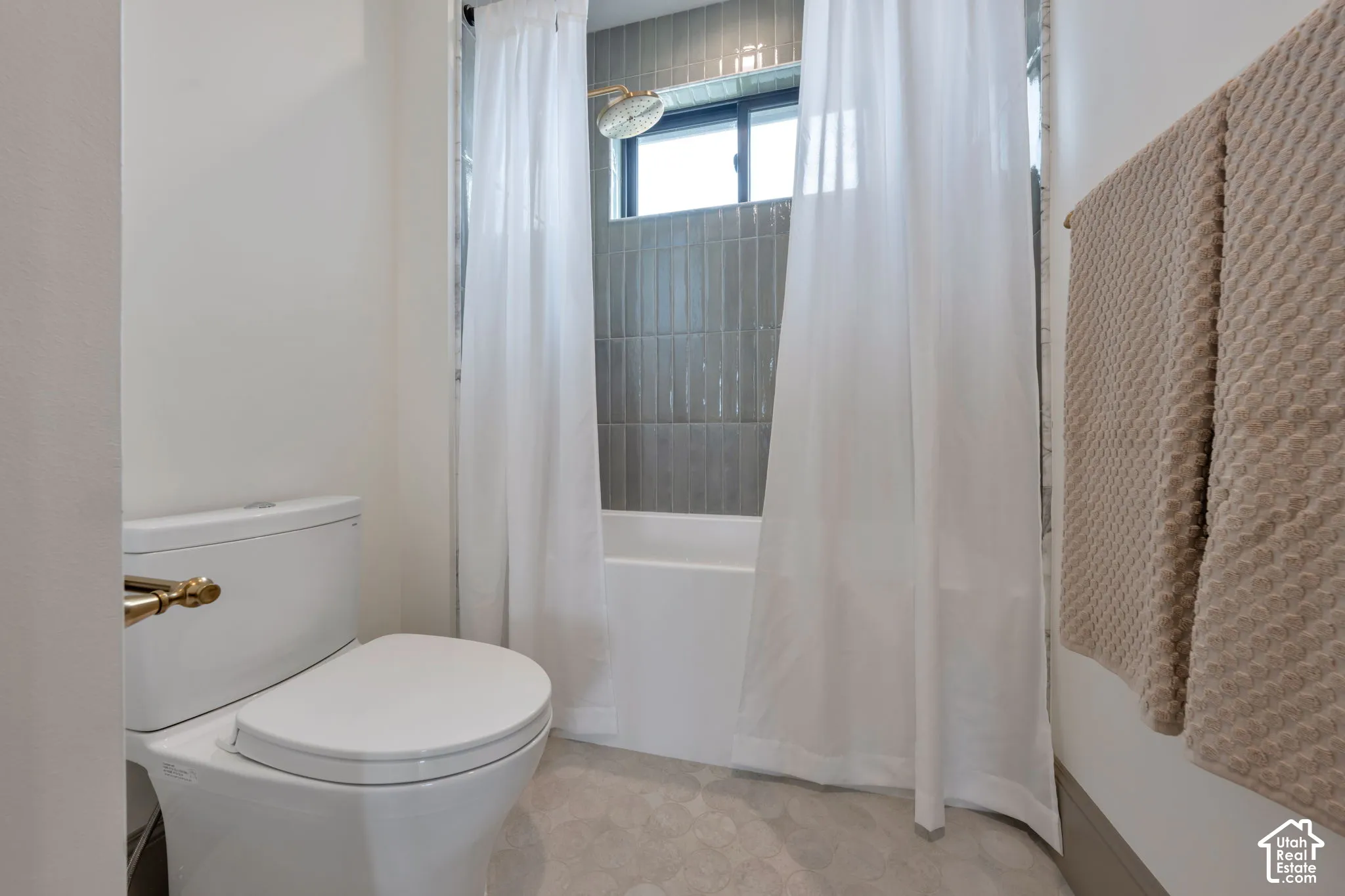 White bathtub with grey vertical tile surround, fixed window, and a wall-mounted shower head