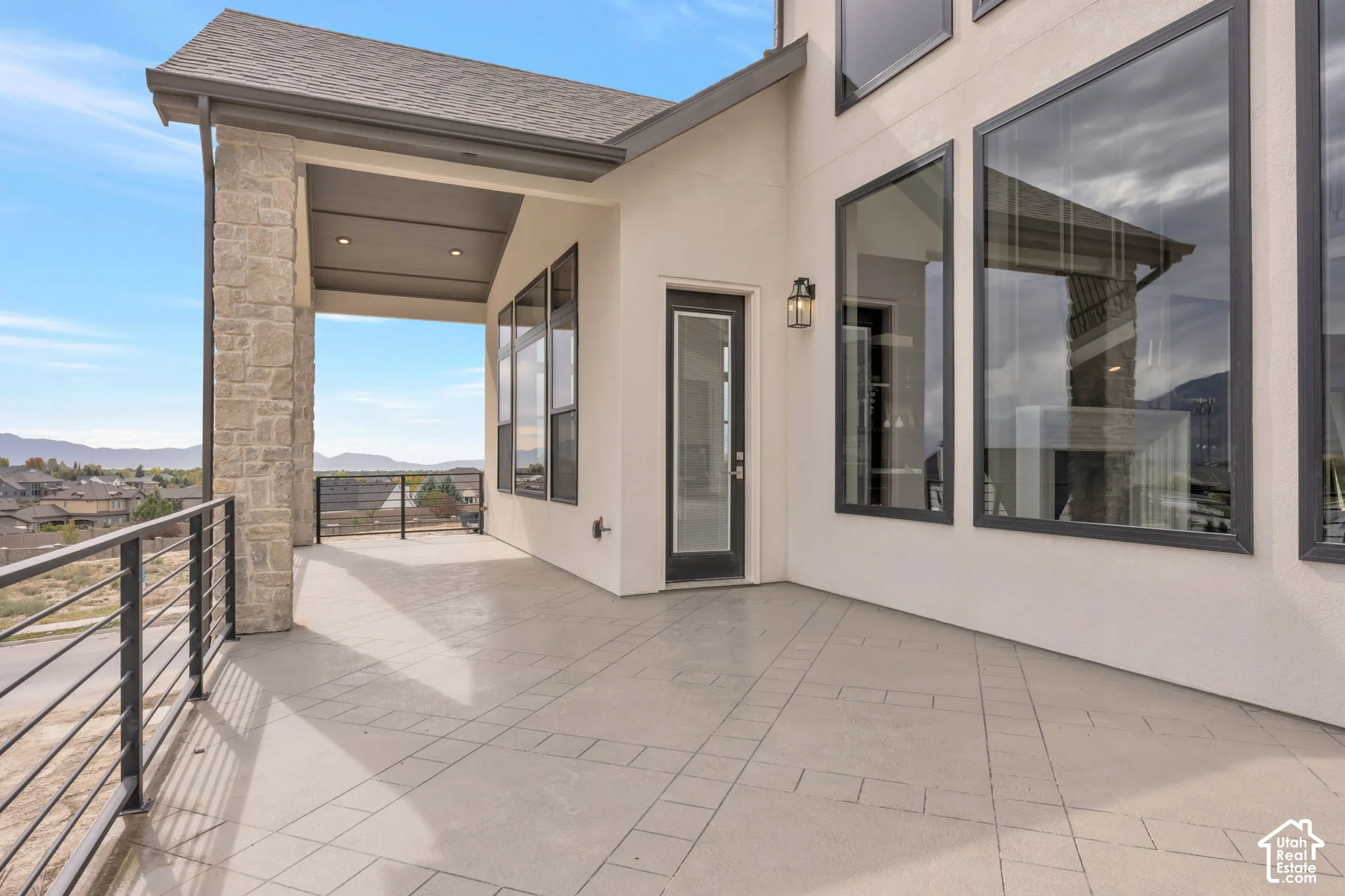 Expansive covered patio featuring stone-clad pillars, a metal railing, and a patterned concrete surface