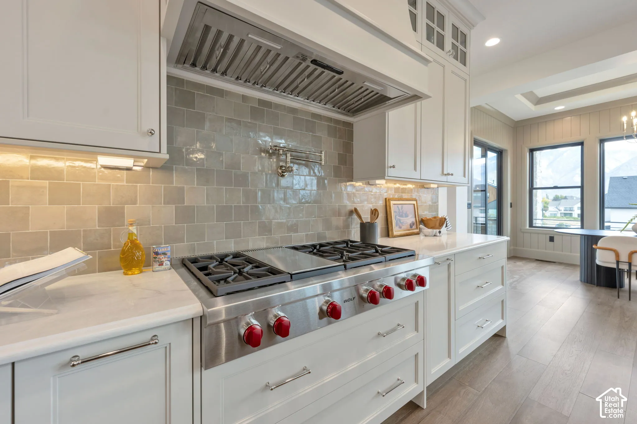 Gourmet kitchen featuring a stainless-steel range, tiled backsplash, white cabinetry, and light-toned flooring