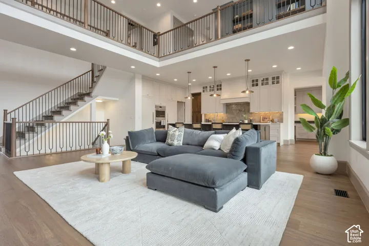 Open-concept living area with high ceilings, wood-finish flooring, and a two-story staircase featuring decorative metal balusters