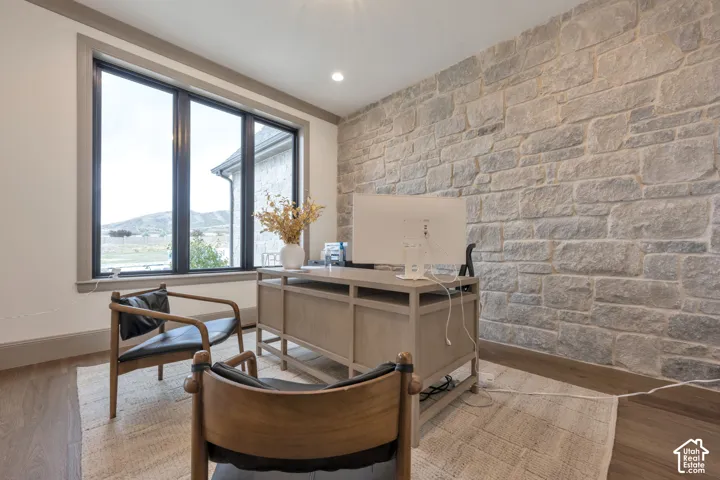 Stone-clad accent wall, recessed ceiling lighting, large window with dark trim, wood-finish flooring
